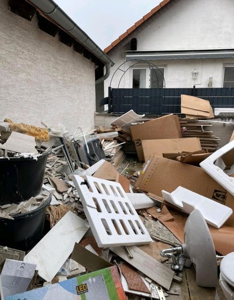 Cluttered driveway with scattered cardboard boxes, broken furniture, and household waste behind a residential house