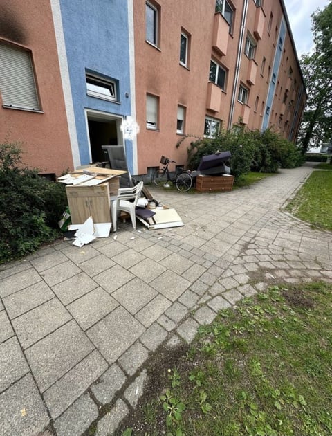 Multi-story brick apartment building with discarded furniture and items scattered on a paved courtyard area