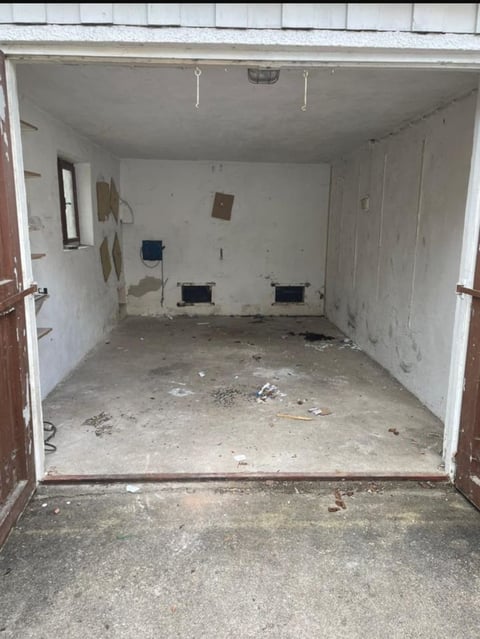 Empty garage interior with concrete floor, white walls, open brown doors, and electrical outlets installed on the walls