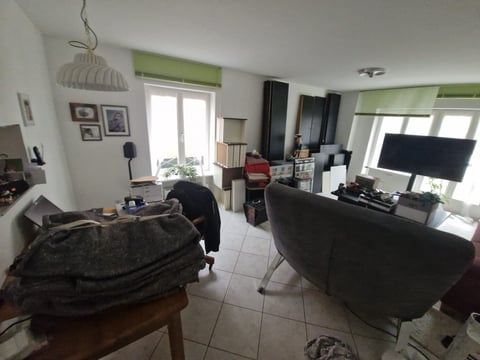 Spacious modern living room with black furniture, large windows with green blinds, and entertainment setup including a flat-screen TV