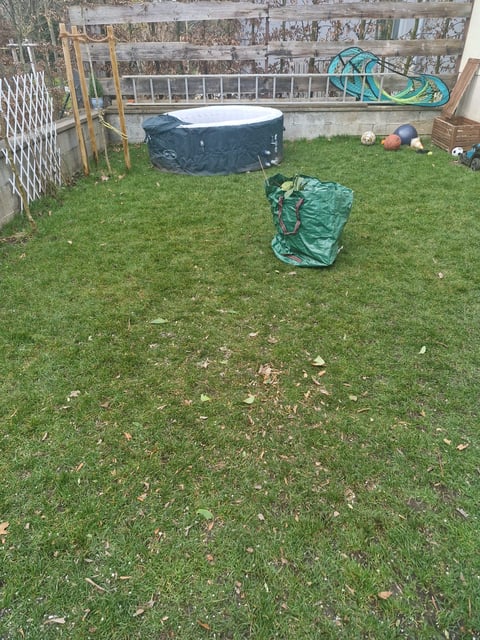 Residential backyard with green lawn, covered hot tub, garden storage bag, sports equipment, and fence with graffiti art in background