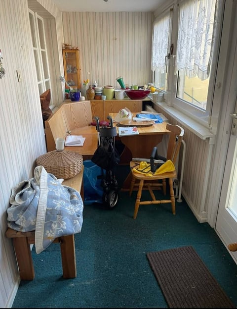 Cluttered home office or utility room with wooden desk, storage items, and large windows